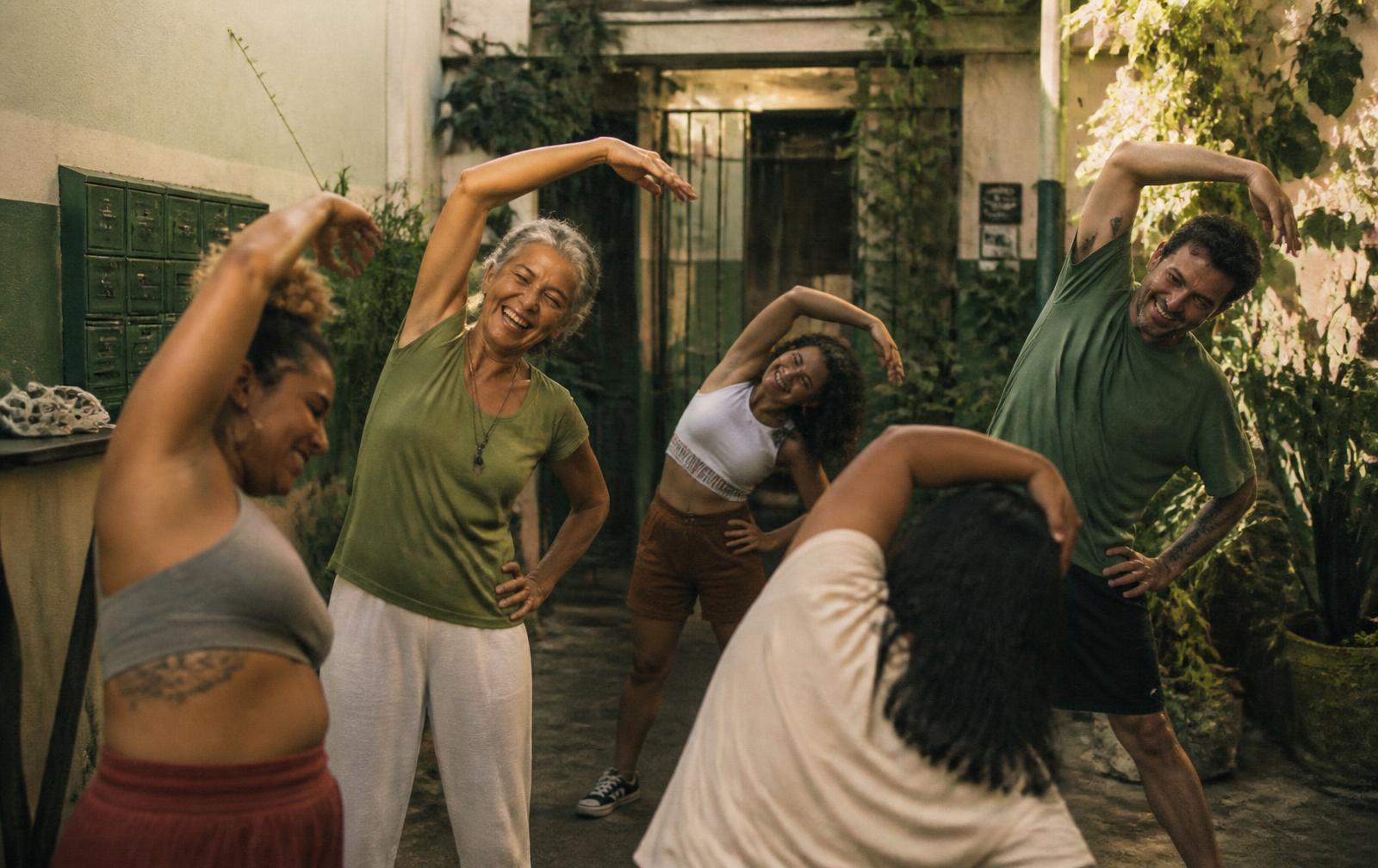 Grupo diverso de brasileiros de idades diferentes se alongando juntos no pátio do prédio